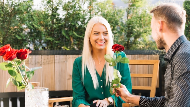 Man sitting at rooftop giving red rose to her smiling girlfriend