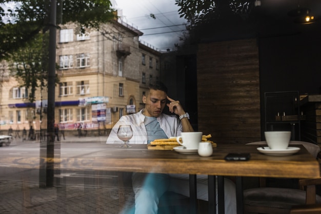 Free Photo man sitting at table in restaurant seen from window glass