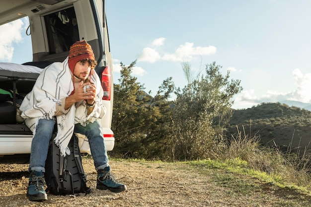 Man sitting on the  trunk of the car while on a road trip with copy space