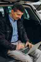 Free photo man sitting in trunk of his car and working on computer