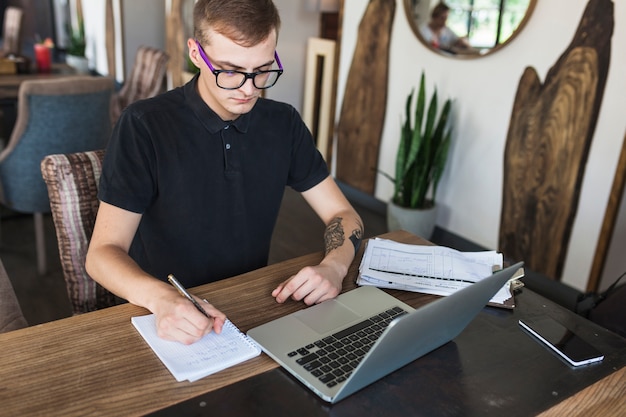 Man sitting with notepad and laptop at table