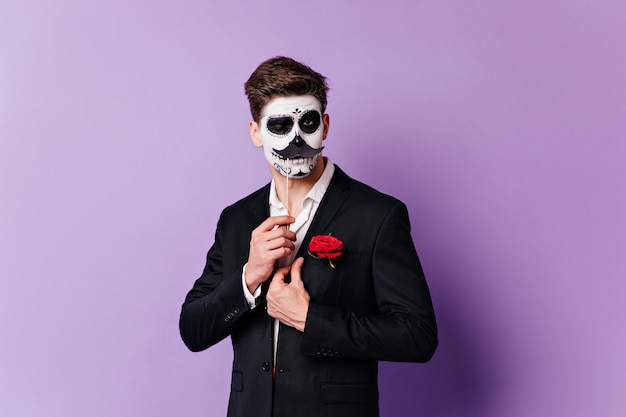 Free photo man in skull mask winks coquettishly, posing with overlaid mustache for portrait on isolated background.