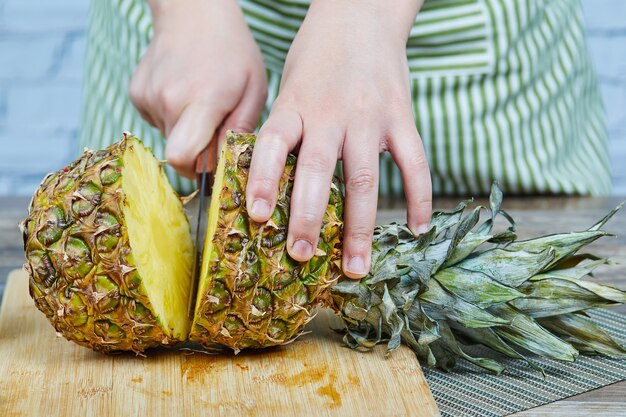 Man slicing a fresh pineapple on a wooden cutting board