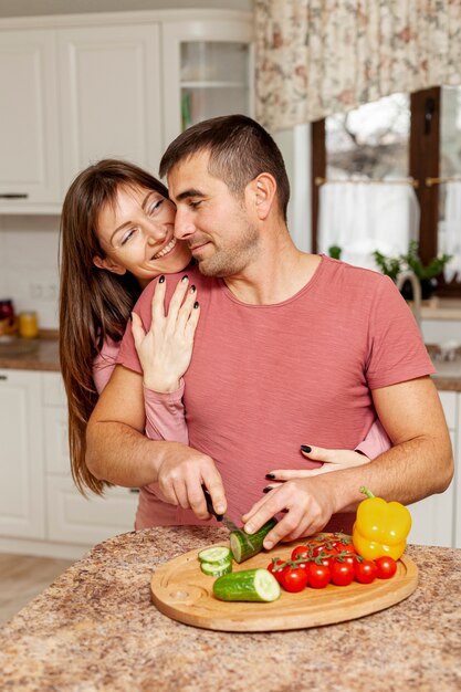 Man slicing vegetables embraced by his girlfriend