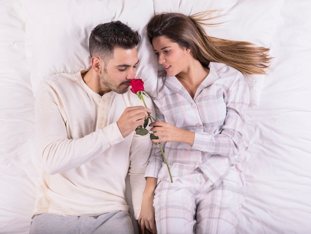 Man smelling rose in bed with woman