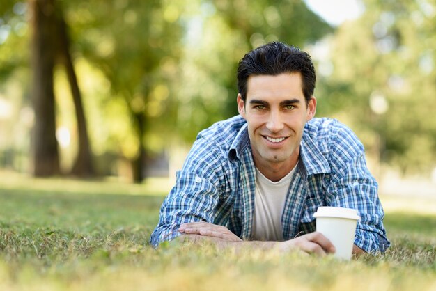 Man smiling lying on the lawn with a coffee