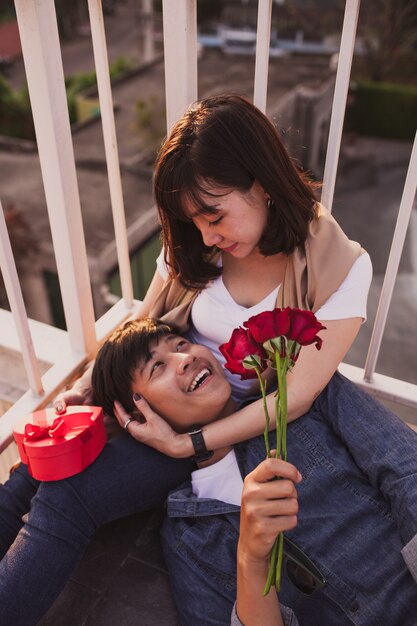 Man smiling lying on the legs of a woman with a bouquet of roses