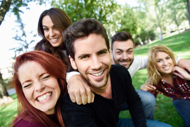 Free photo man smiling taking a self photo of him and his friends with a park in the background