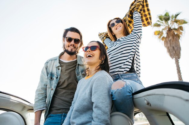 Man and smiling women with upped hands leaning out from car