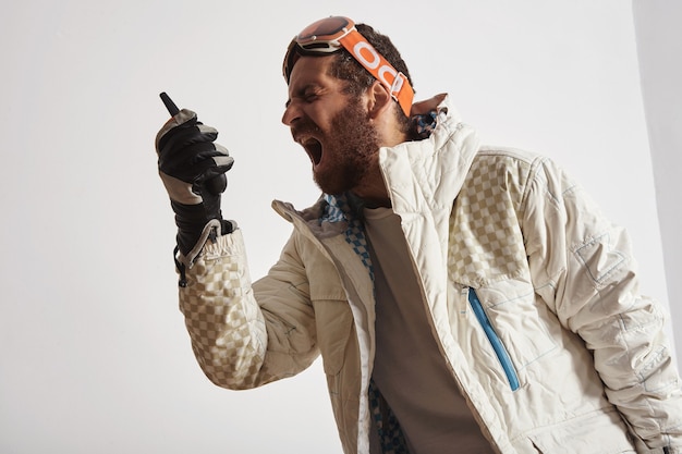 Man in snowboard gear with goggles on head screaming into walkie talkie