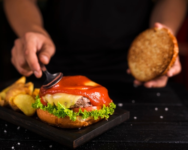 Man spreading ketchup on tasty beef burger