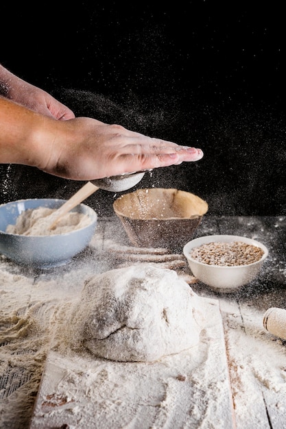 Free photo man sprinkling flour over fresh dough on kitchen table