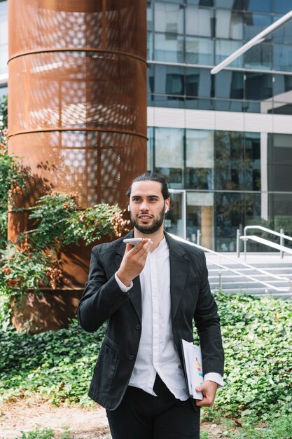 Man standing in front of building holding mobile phone in hand and talking on loudspeaker