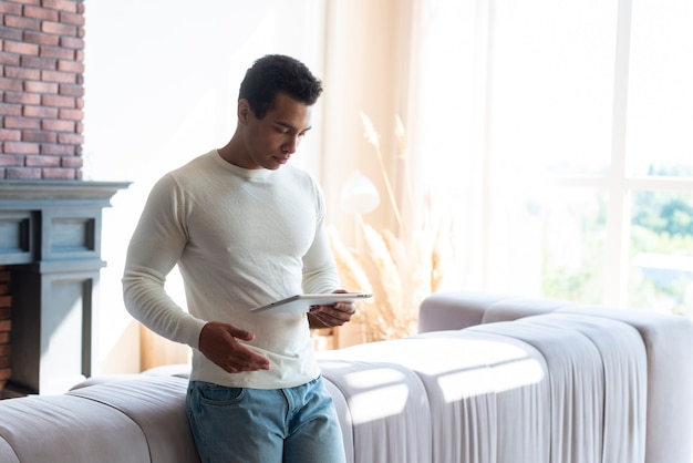 Free Photo man standing in living and holding tablet