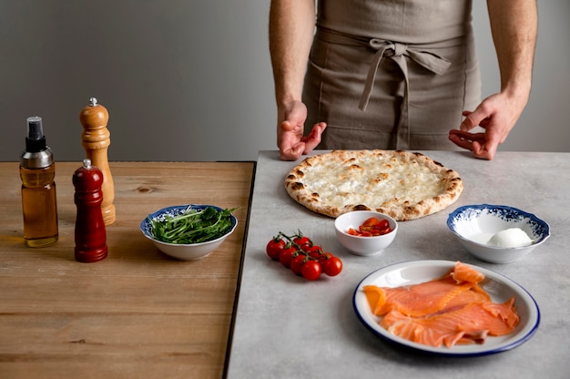 Free photo man standing near baked pizza dough and ingredients