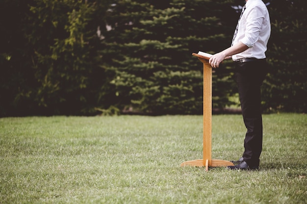 Free photo man standing near a wooden stand with a book on it in the park