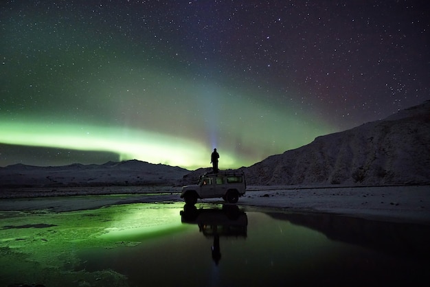 Free photo man standing on suv watching northern lights