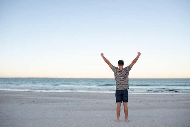 Free photo man standing with arms outstretched on the beach