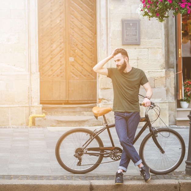 Free photo man standing with his bicycle on sidewalk