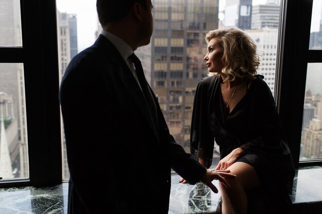 Man stands before a stunning woman looking through the panoramic window at New York streets