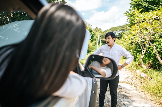 Free photo a man stands looking at a broken car and a woman sits in it.