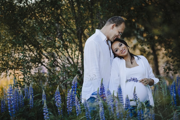 Man stands sideway and his pregnant wife leans to him, they smile