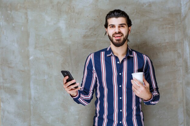 Man in striped shirt holding a water cup and playing with his phone