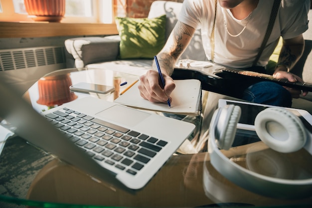 Free photo man studying at home during online courses or free information by hisself. becomes musician, guitarist while isolated, quarantine against coronavirus spreading. using laptop, smartphone, headphones.