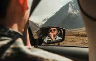 Free photo man in sunglasses looking at the mountains with car window reflected in the mirror