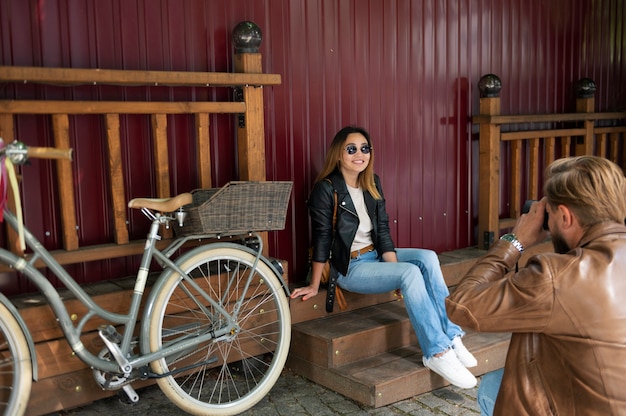 Free photo man in synthetic leather jacket taking photo of his girlfriend outdoors