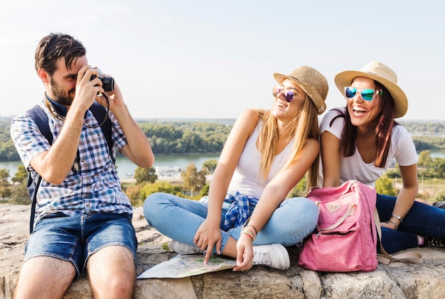 Free photo man taking photo of two happy fashionable women on camera