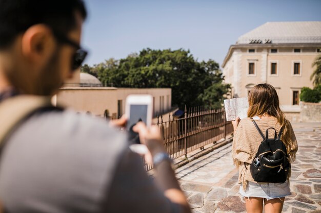 Man taking photograph of woman looking at map standing on street