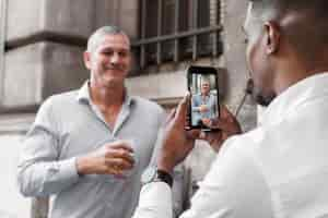 Free photo man taking photos of friend with smartphone