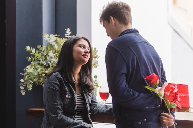 Free photo man talking to his girlfriend and hiding on his back a gift and a rose