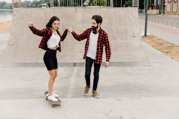 Free photo man teaching girlfriend to ride a skateboard