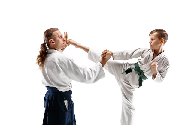 Free photo man and teen boy fighting at aikido training in martial arts school. healthy lifestyle and sports concept. fightrers in white kimono on white wall. karate men with concentrated faces in uniform.