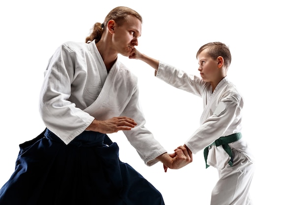 Man and teen boy fighting at Aikido training in martial arts school. Healthy lifestyle and sports concept. Fightrers in white kimono on white wall