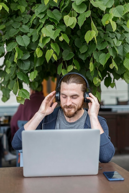 Free photo man at a terrace listening to music on headphones with laptop