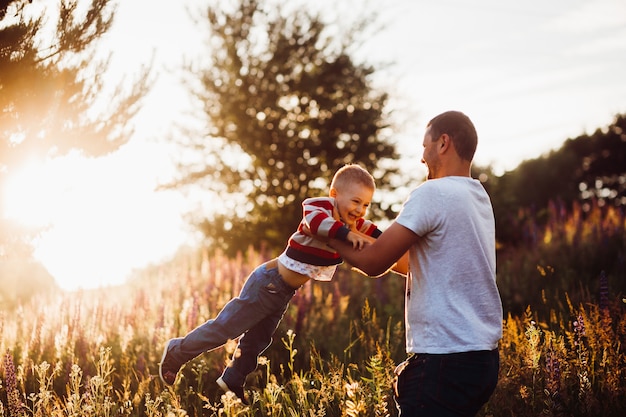 Free photo man throws his son up posing on the field in lights of evening sun