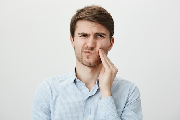 Man touching cheek and grimacing from pain from toothache, need dentist