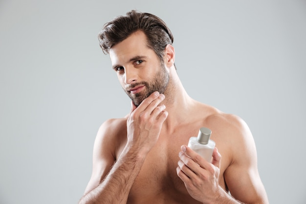 Man touching his face while holding bottle of perfume