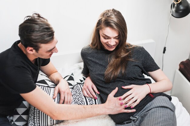 Man touching pregnant woman's belly in bedroom