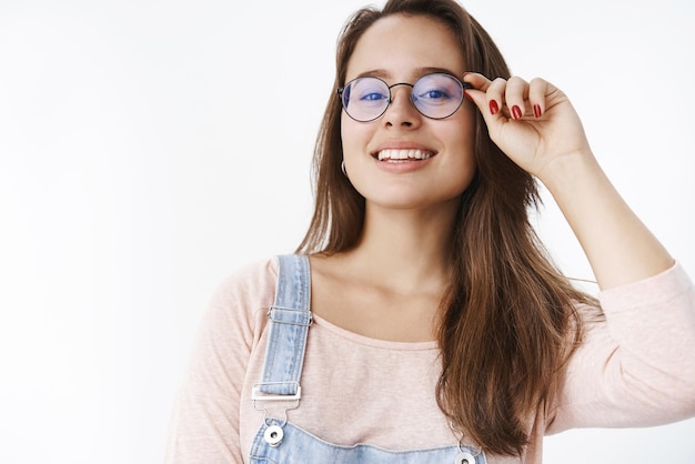 man touching rim of glasses and smiling proudly, being ambitious and delighted of living by her rules on gray wall.