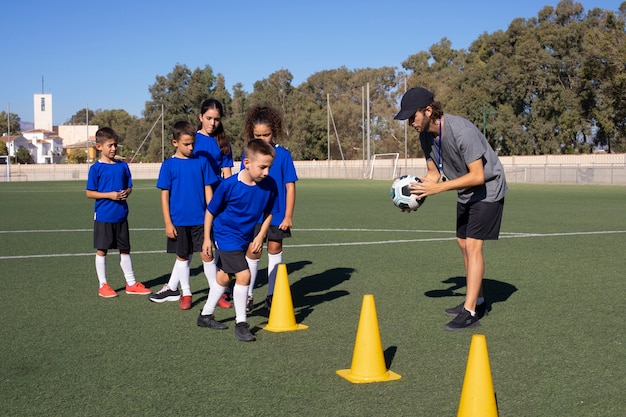 Man training kids playing football  full shot