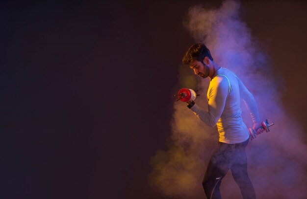 Man training with dumbbells in colored steam