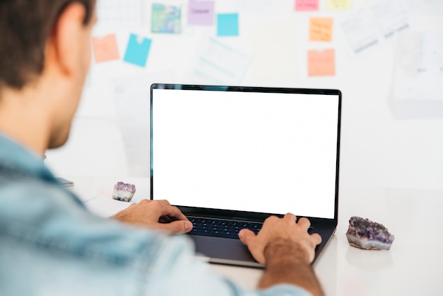 Free Photo man typing on laptop at desk near wall with notes