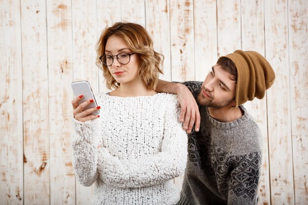 Man unnerve his girlfriend looking at phone over wooden wall