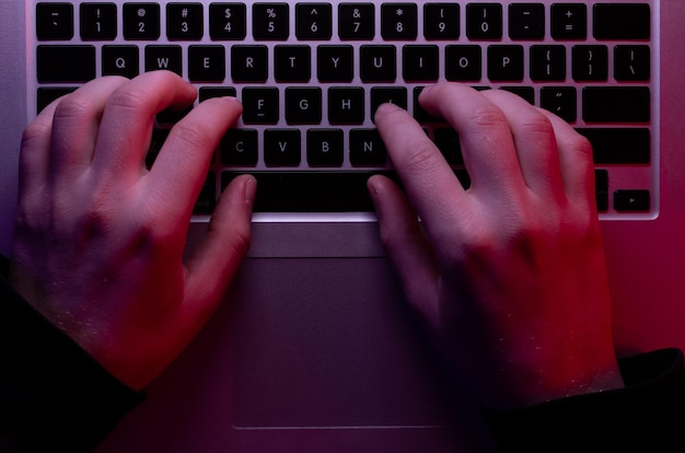 Free Photo a man uses a laptop closeup male hands in neon lighting top view