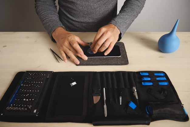 Man uses vacuum plug to remove screen from broken phone, his toolkit with special tools near