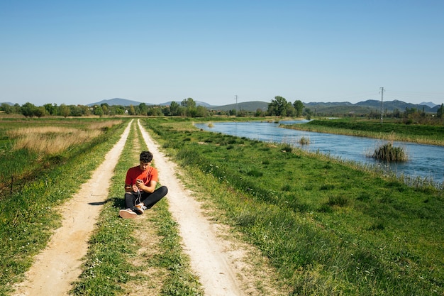 Free photo man using cellphone siting on diminishing pathway